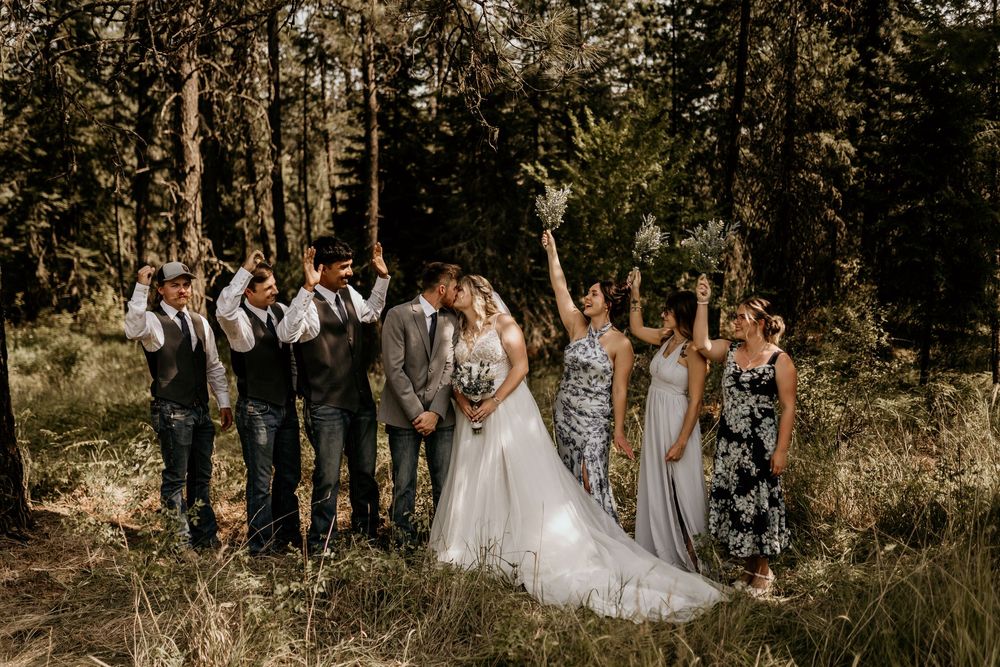 Wedding party celebrates in a rustic outdoor forest setting with pine trees.