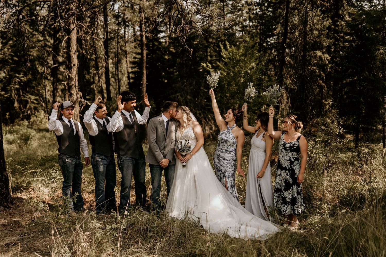 Wedding party celebrates in a rustic outdoor forest setting with pine trees.
