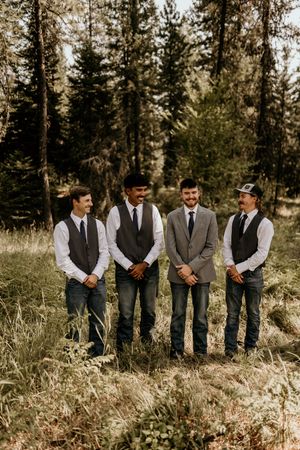 Groomsmen in vests and suits stand together in a wooded mountain setting.