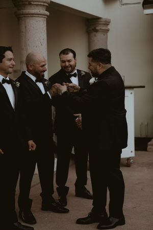 Groomsmen in black tuxedos gather and share laughs during a wedding celebration.