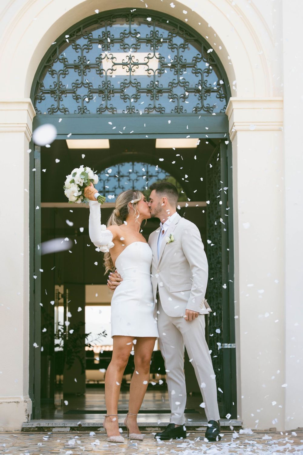 Couple celebrating their wedding with confetti shower under elegant white archways at a classic venue.