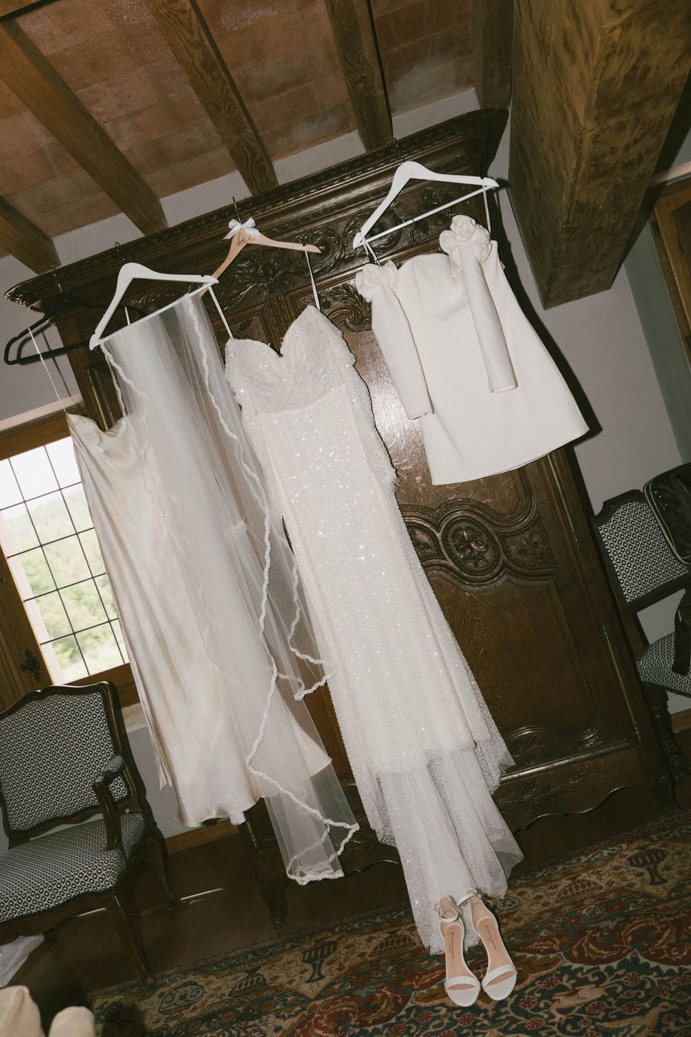 A white wedding dress and shoes displayed in a rustic room with exposed wooden beams and natural lighting.