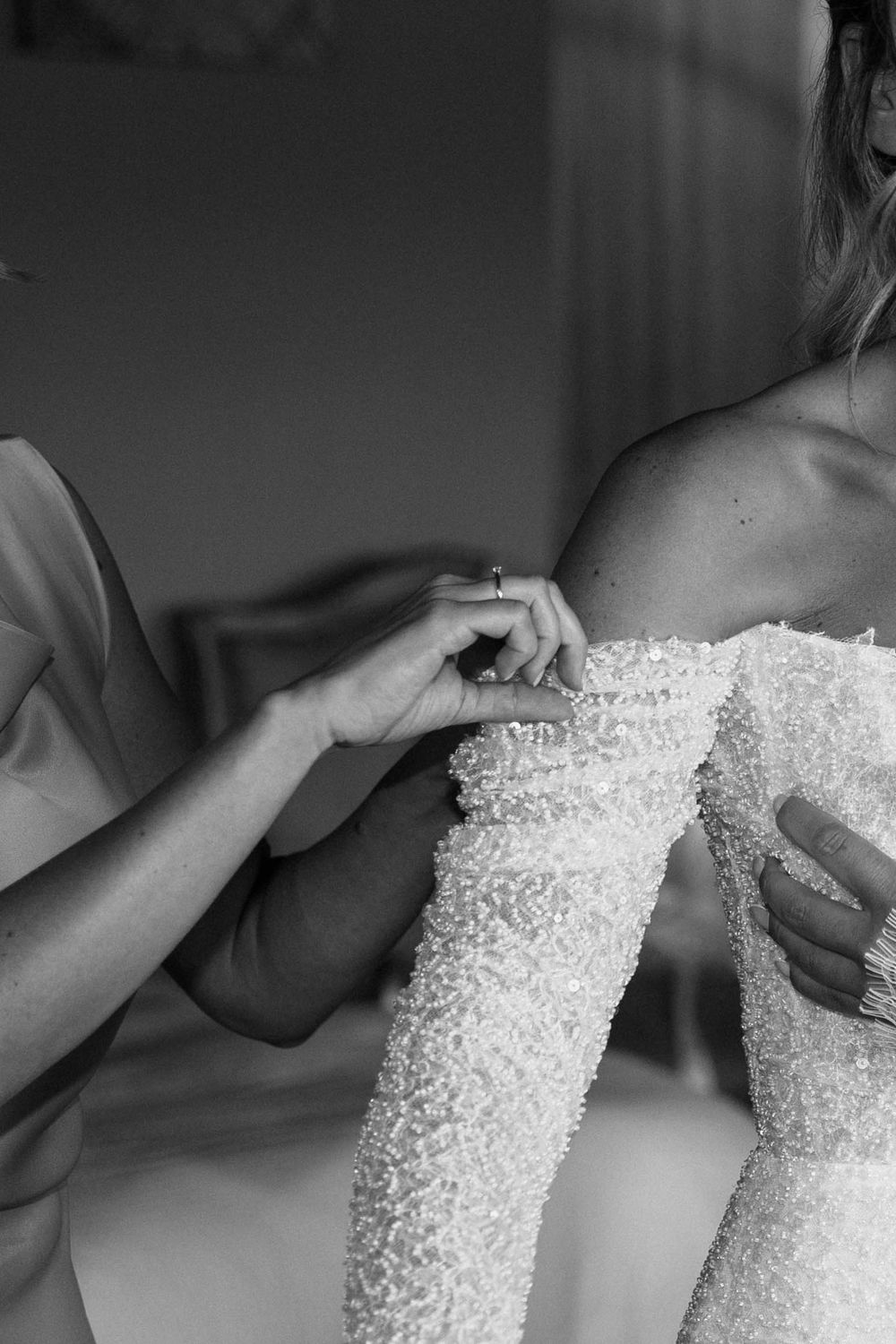Une série d'images en noir et blanc montrant les mains ajustant et ajustant un délicat corsage de robe de mariée perlé.
