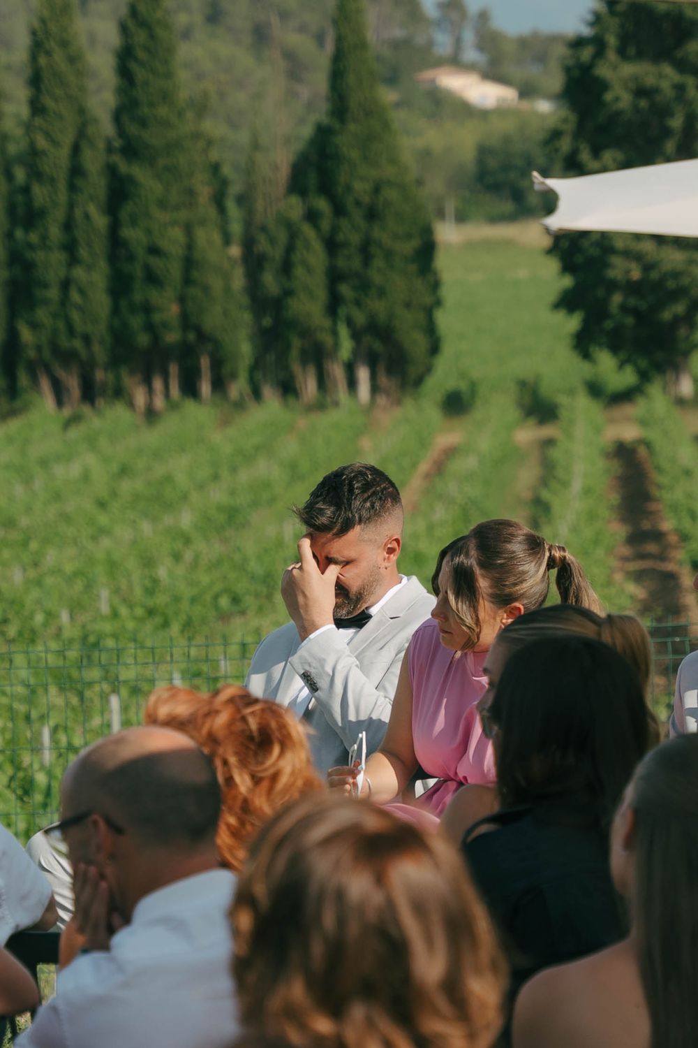 A group of people gathered at a vineyard for wine tasting with rows of grapevines visible in the background.