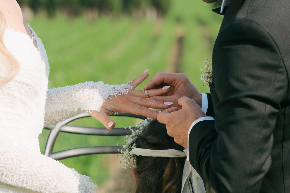 A couple in formal wedding attire cuts their white tiered wedding cake together during an outdoor reception.
