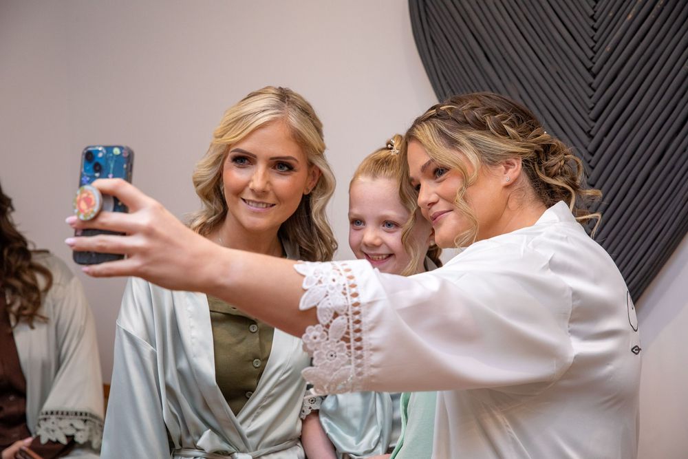 Two women and a young girl take a selfie together while getting ready for a wedding celebration.