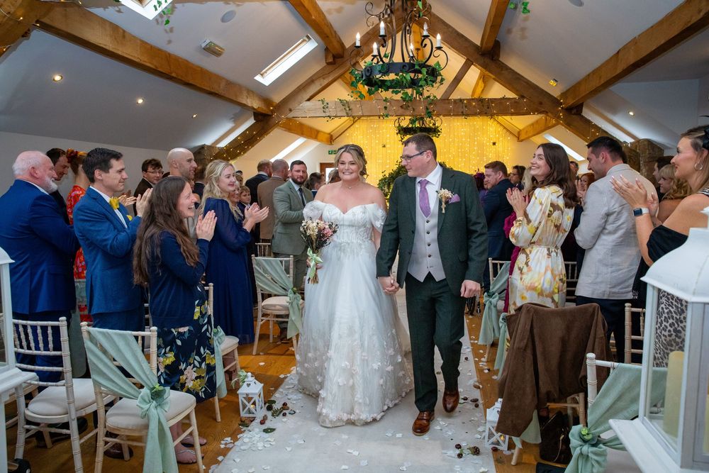 Newlywed couple walks back down the aisle through confetti in a stunning rustic barn wedding venue.