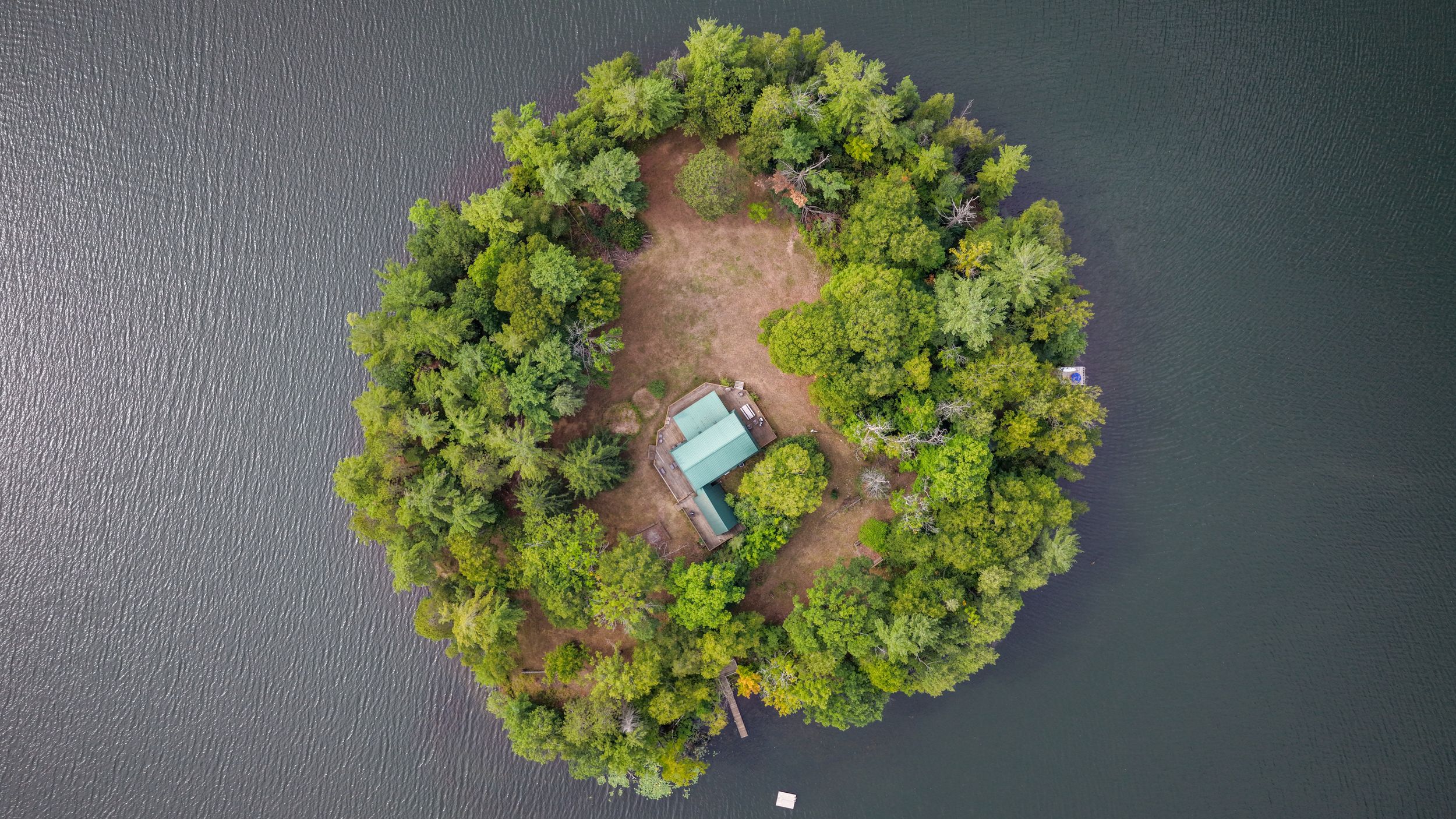 Aerial view of a small lush green island with a cabin surrounded by calm water.