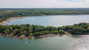 Aerial view of a serene lake surrounded by lush green trees with docks and boats along the shoreline.
