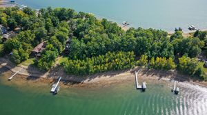 Aerial view of a lush green wooded lakeside property with two boat docks extending into calm blue water.