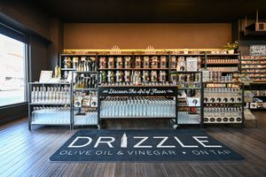 Interior of Drizzle Olive Oil & Vinegar On Tap store with shelves of bottles and branded floor sign.