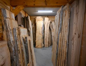 Large collection of raw wood slabs stored vertically in a wooden storage facility with overhead lighting.