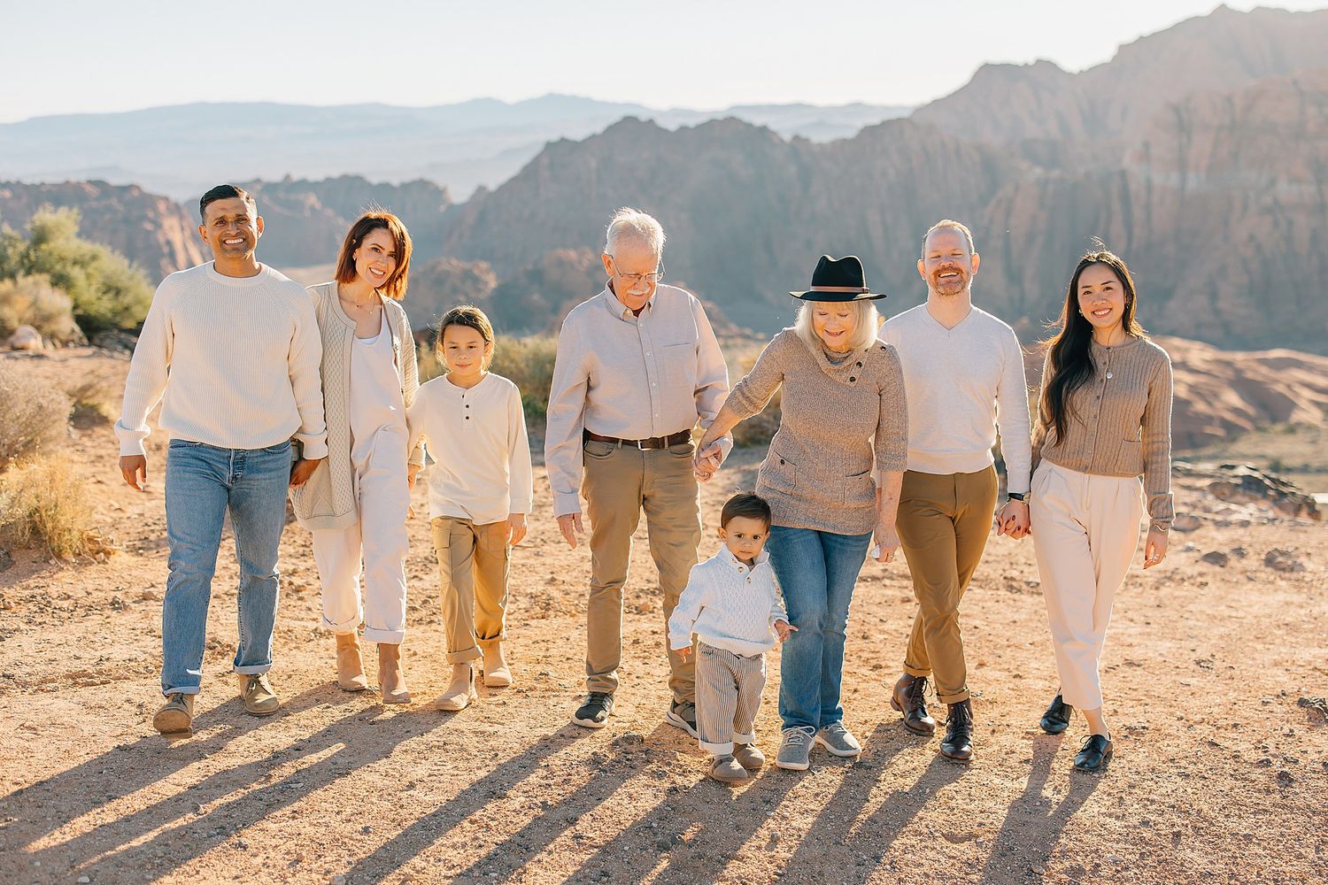 Multigenerational family walking together in a sunny desert setting with rocky mountains behind them.