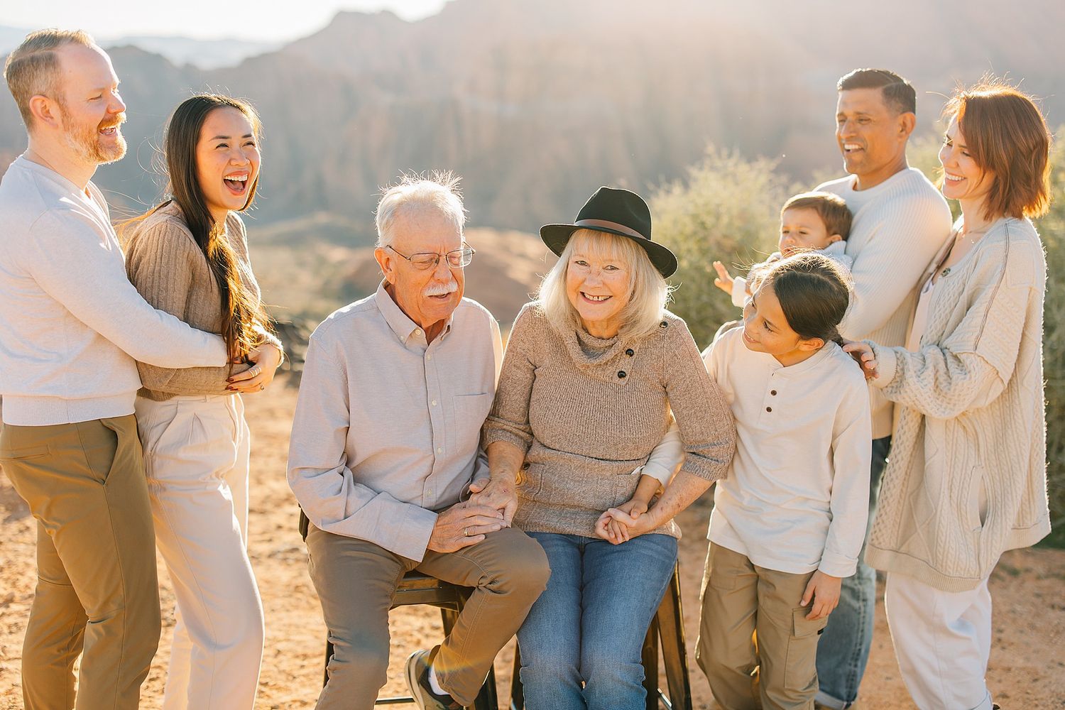 Multi-generational family laughing together outdoors in golden hour light with desert mountains in the background.
