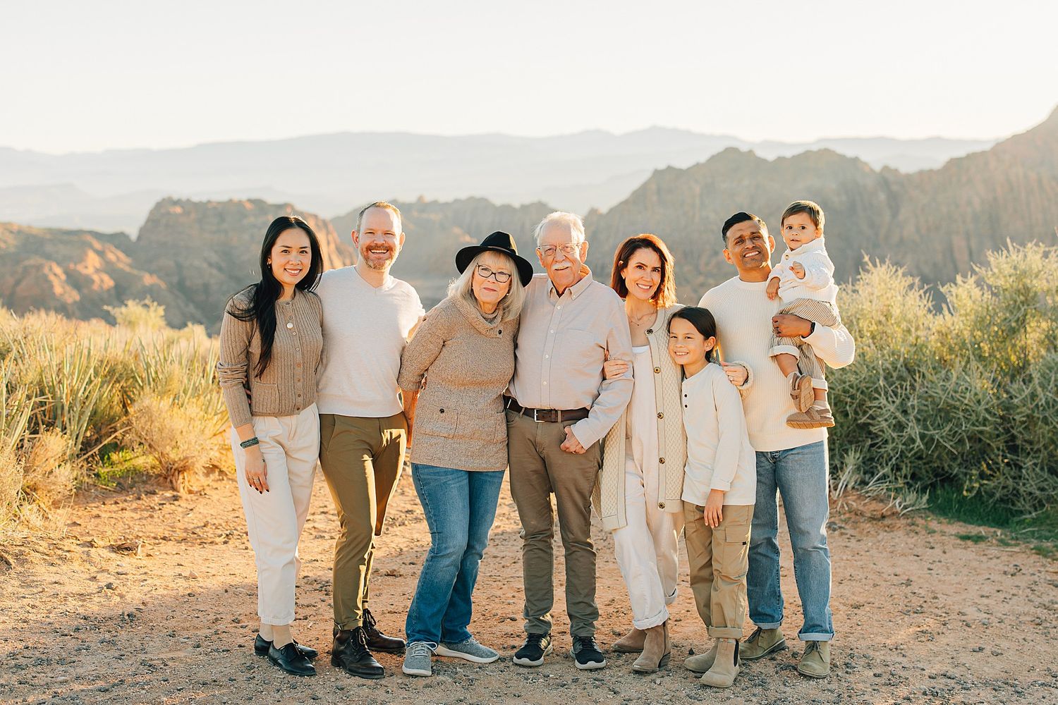 Multi-generational family posing together outdoors with scenic mountain canyon views in warm golden sunlight.