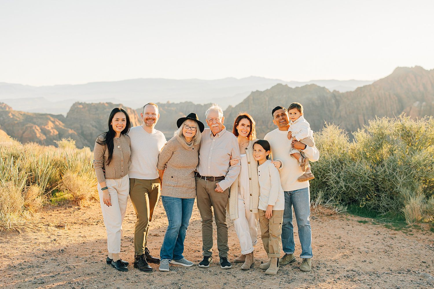 Extended family group photo outdoors with scenic mountain backdrop in soft natural light.