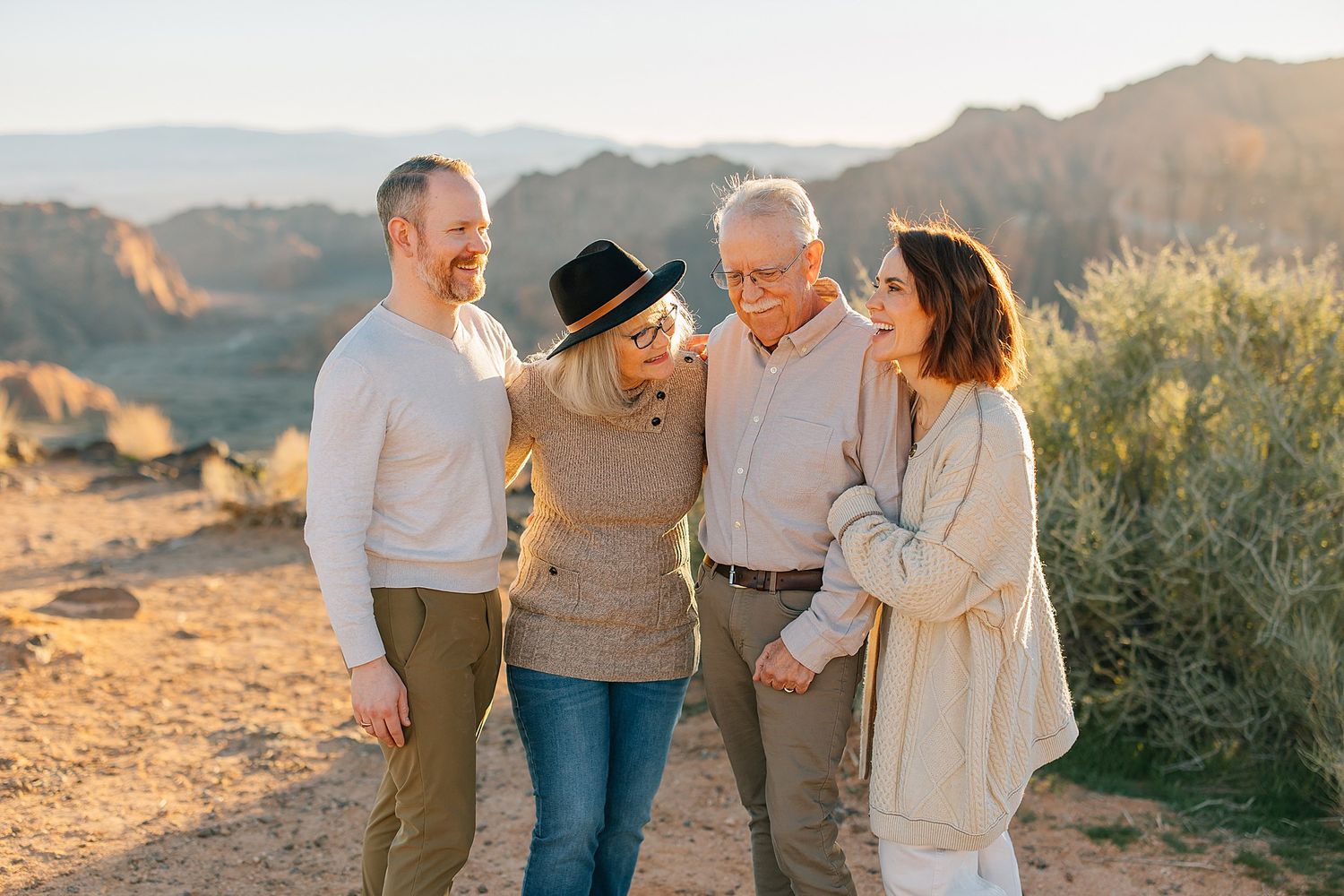 Four adults laugh together outdoors at golden hour with desert mountains in the background.