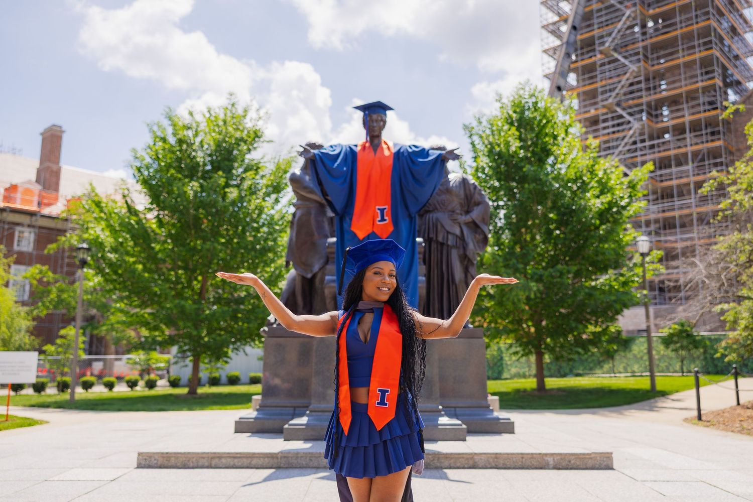 Girl graduate posing in front of Alma Mater dressed in graduation attire