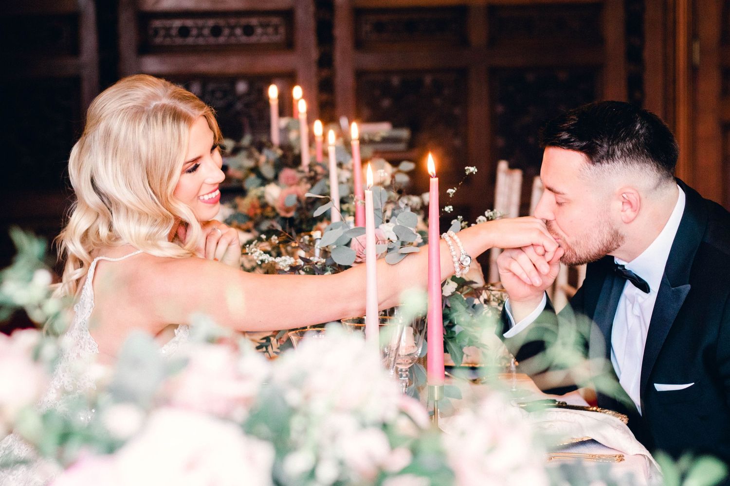 Romantic candlelit dinner scene with couple seated at elegant table with floral centerpiece and glowing candles.