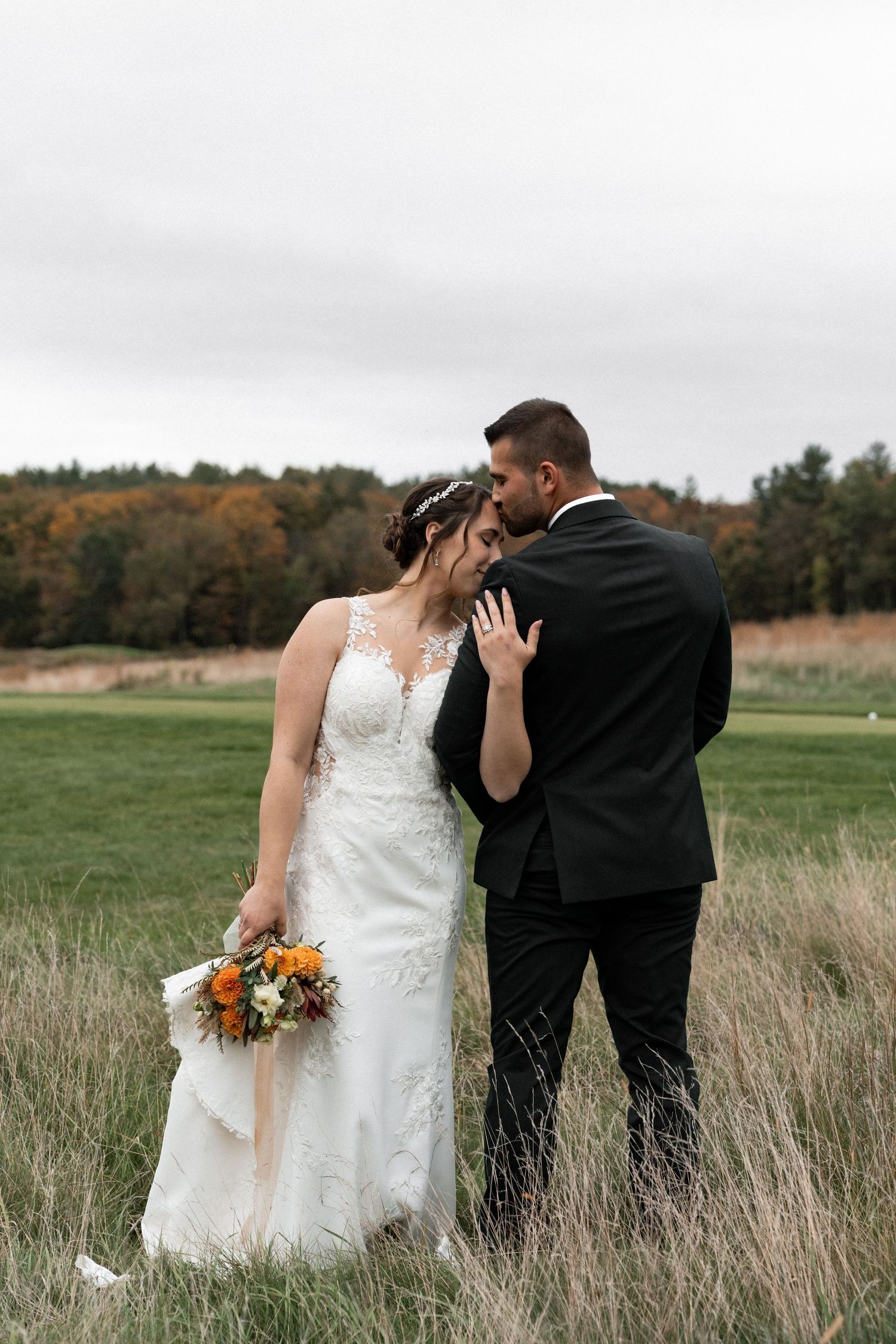 A romantic wedding couple shares intimate moments in a rustic field with autumn foliage in the background.