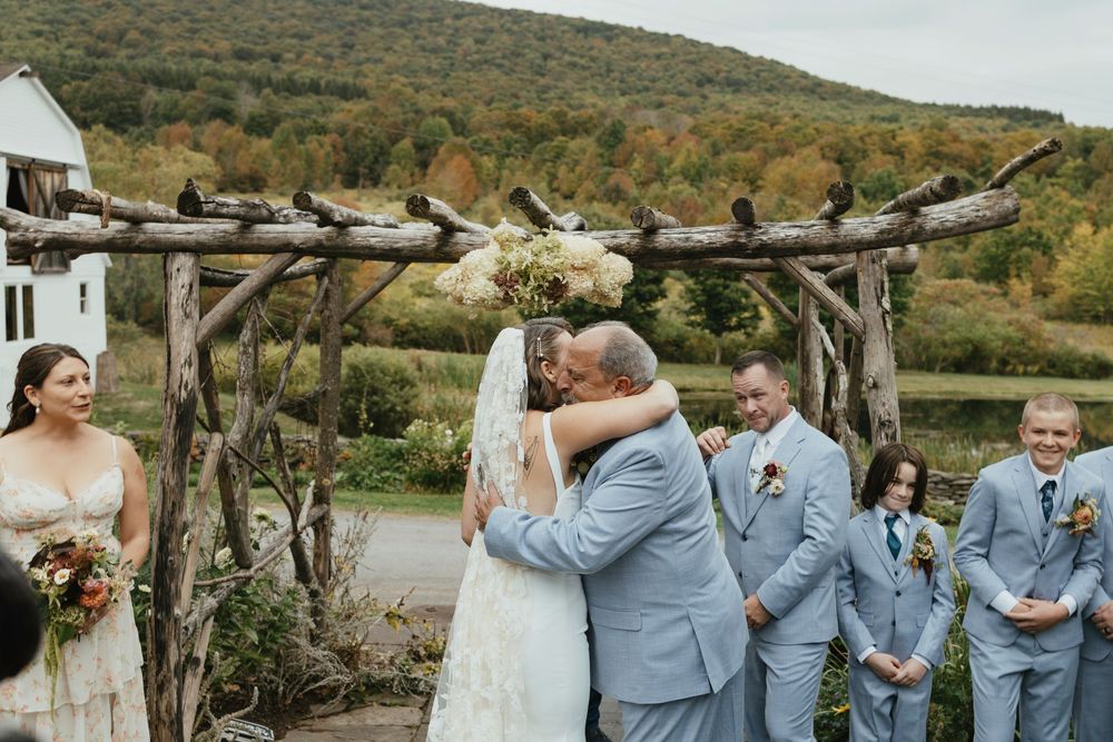 Wedding party in light blue attire poses together outdoors against a scenic autumn mountain backdrop.