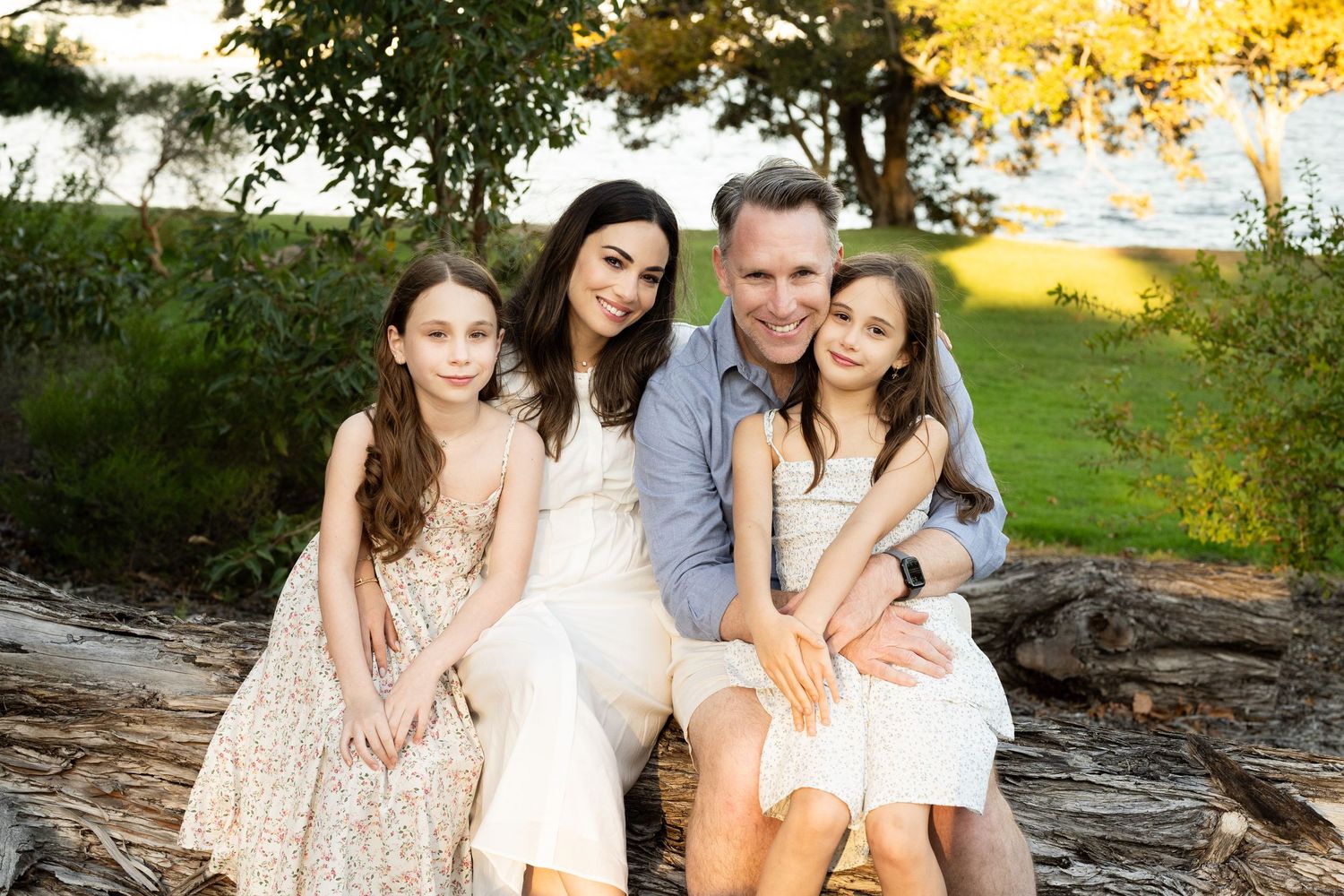 A father, mother and two children sitting on a log outdoors smiling together during a Perth family photography session