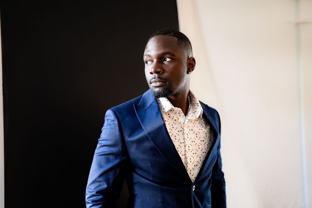 Stylish man in blue blazer and patterned shirt posing confidently against a black and white background.