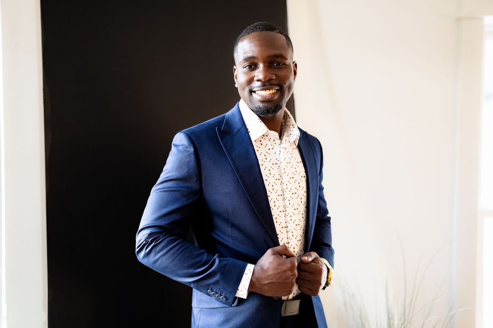 Smiling man in navy blue suit and floral shirt posing confidently indoors.