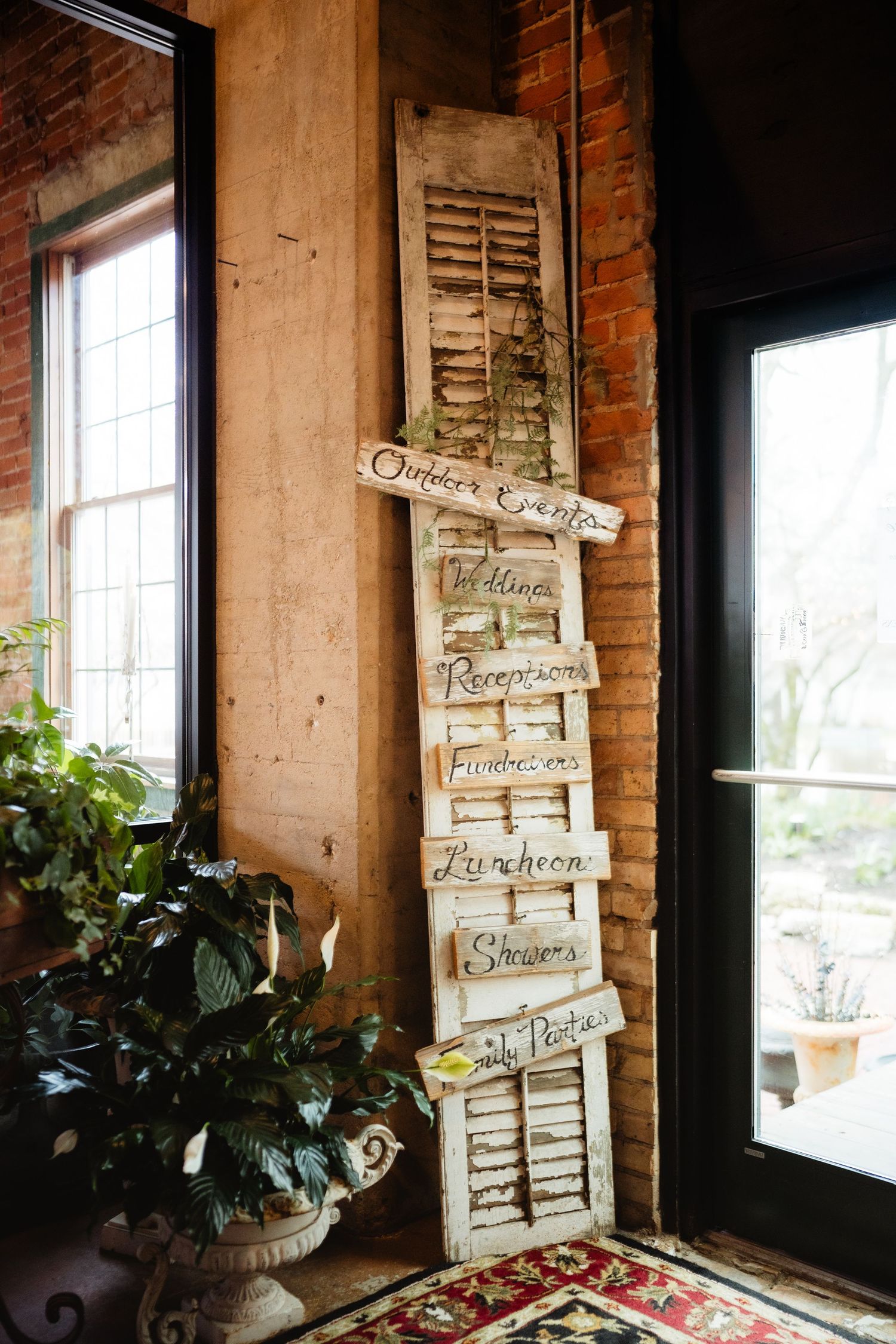 Rustic wedding venue decor featuring vintage shutters with handwritten event signs leaning against a brick wall.