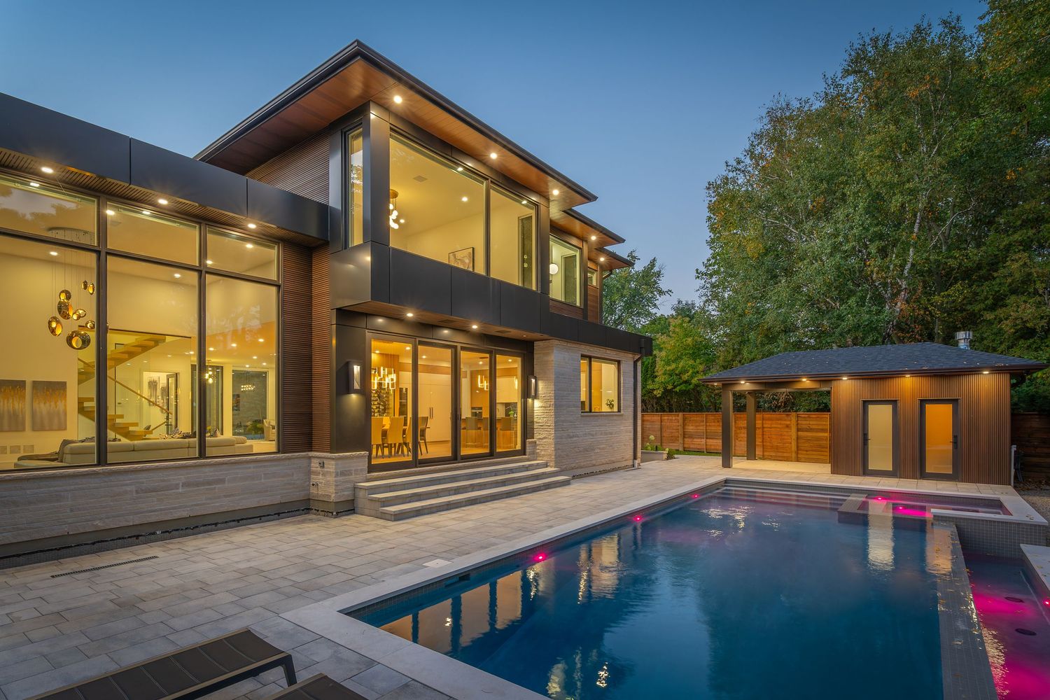 Modern luxury home exterior with illuminated windows and backyard swimming pool at twilight.