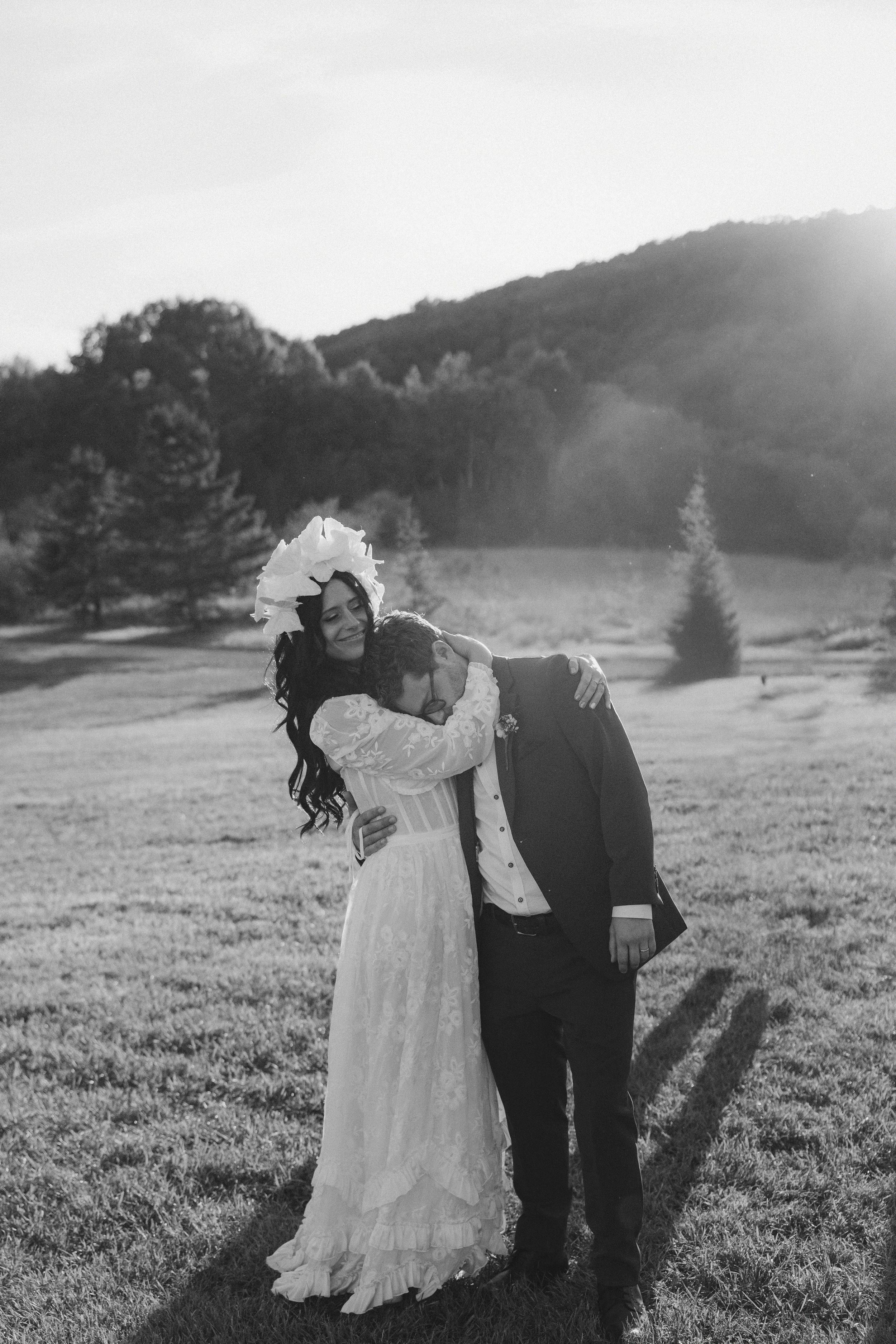 A romantic couple embraces in a sunlit meadow with rolling hills in black and white photography.