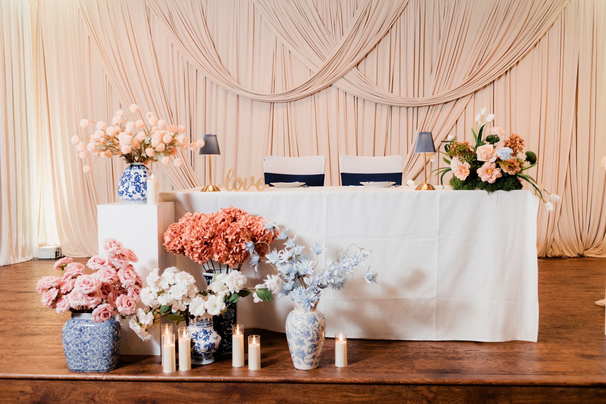 Elegant sweetheart table decorated with peach and pink floral arrangements in blue and white vases.