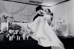 Groom lifts bride in wedding dress during romantic first dance at elegant wedding reception.