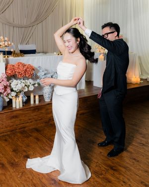 Groom spins bride in strapless wedding gown during first dance at floral-decorated reception.