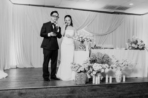 Bride and groom stand together giving speech at wedding reception with floral arrangements.