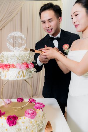 Smiling couple cuts elegant floral wedding cake decorated with pink roses and Mr & Mrs topper.