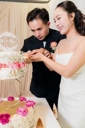Bride and groom together slice their multi-tiered floral wedding cake at reception celebration.