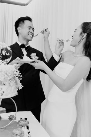Bride and groom playfully feed each other wedding cake at their elegant reception celebration.