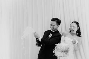 Joyful bride and groom laughing together during their wedding celebration against a white draped backdrop.