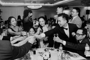 Wedding guests joyfully toasting with drinks at a lively Asian wedding reception banquet table.