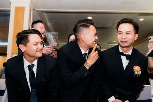 Three groomsmen in black tuxedos sharing a lighthearted moment together at the wedding reception.