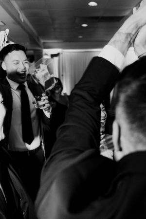 Excited wedding guest laughing and toasting with drinks during a lively wedding reception celebration.
