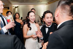 Bride and groom sharing a joyful moment laughing with wedding guests during their reception.
