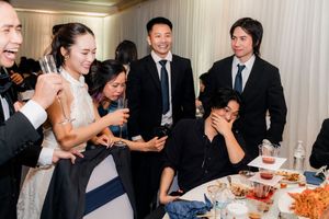 Wedding guests laughing and toasting with champagne glasses at a reception dinner table.