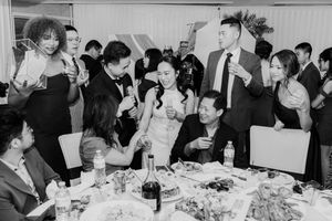 Black and white photo of wedding guests celebrating and toasting at a reception dinner table.