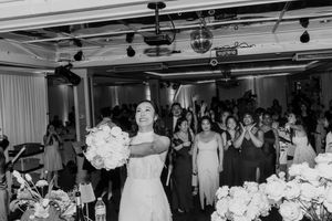 Bride tossing her white bouquet to guests at wedding reception in black and white.