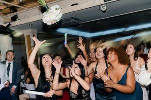 Excited wedding guests reaching up to catch the bridal bouquet toss at reception.