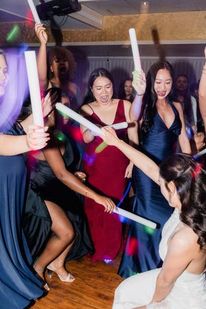 Bride and bridesmaids dancing with colorful glow sticks at lively wedding reception.
