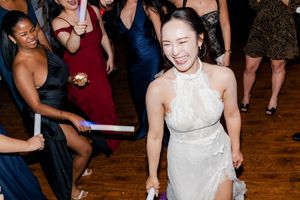 Bride in white halter gown laughing and dancing with guests holding glow sticks at wedding reception.