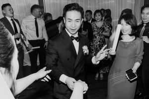 Black and white photo of groom in tuxedo dancing and shaking hands with wedding guests.